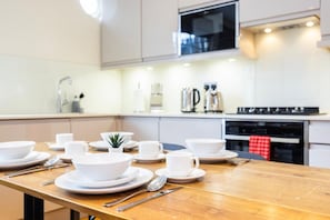 A modern kitchen with a wooden table set for dining, equipped with white plates, cups, and cutlery. - Fitzrovia 1BR Retreat | Near Soho & Tube-13 (Greater London)