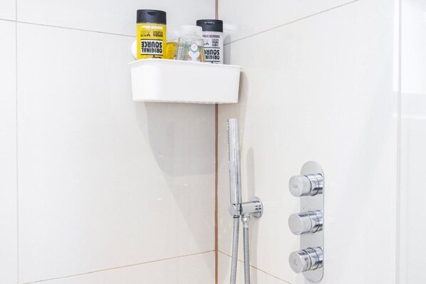 Een badkamer met een witte betegelde muur, een douche met chroombeslag en een plank met toiletartikelen.