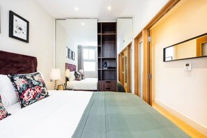 A hotel room with a bed, a bedside table, a lamp, a wardrobe, and a mirror. - Fitzrovia 1BR Retreat | Near Soho & Tube-13 (Greater London)