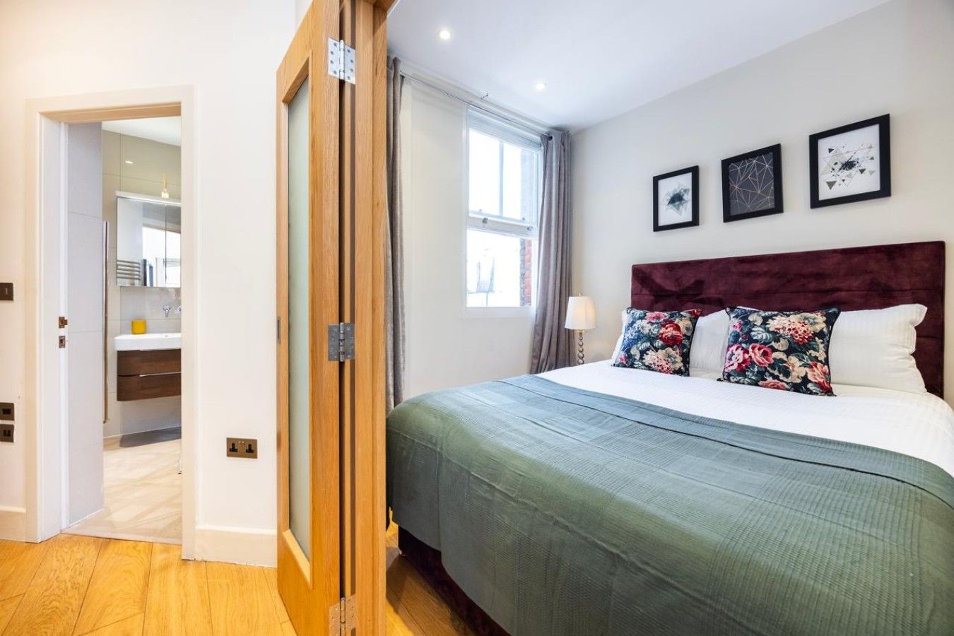 A hotel room with a bed, a wooden door, a window, and a bathroom visible through an open door.