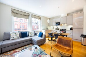 A modern living room with a grey sofa, a glass coffee table, and a dining area with chairs. - Fitzrovia 1BR Retreat | Near Soho & Tube-13 (Greater London)