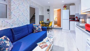 A compact living space with a blue sofa, a dining table with chairs, a kitchen area with a refrigerator, and a staircase leading to an adjacent room. - Stylish 3BR | 3 En-Suite Showers | Sleeps 8 (Greater London)