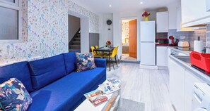 A compact living space with a blue sofa, a dining table with chairs, a kitchen area with a refrigerator, and a staircase leading to an adjacent room. - Stylish 3BR | 3 En-Suite Showers | Sleeps 8 (Greater London)