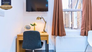 A modern room with a desk, chair, TV, and a window with curtains. - Stylish 3BR | 3 En-Suite Showers | Sleeps 8 (Greater London)