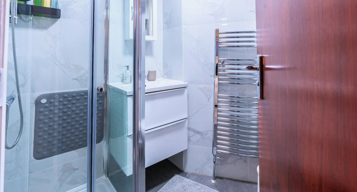 A bathroom with a glass shower enclosure, a white sink, and a chrome towel rack.