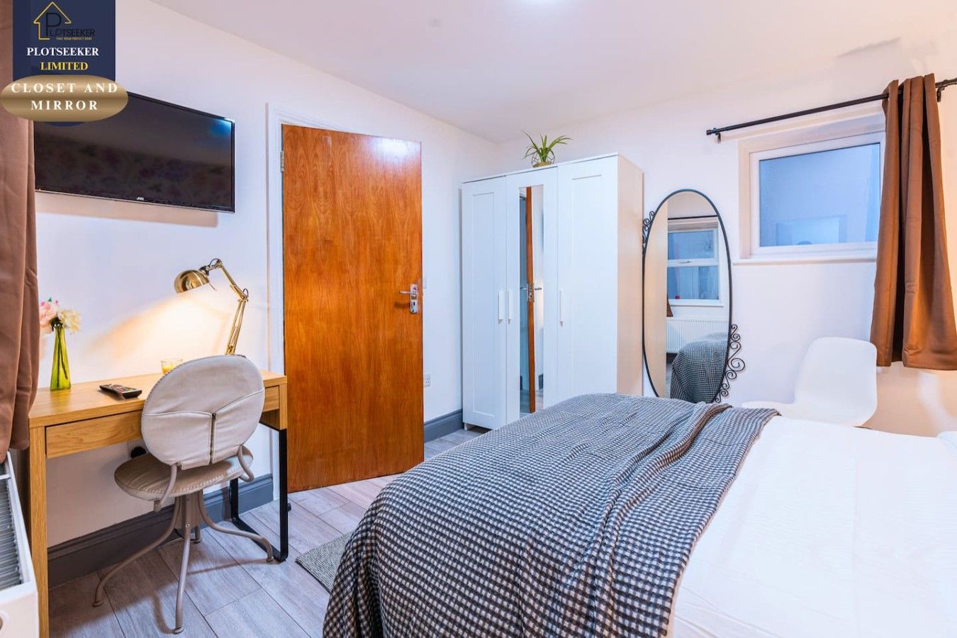 A hotel room with a bed, desk, chair, TV, wardrobe, and a mirror.