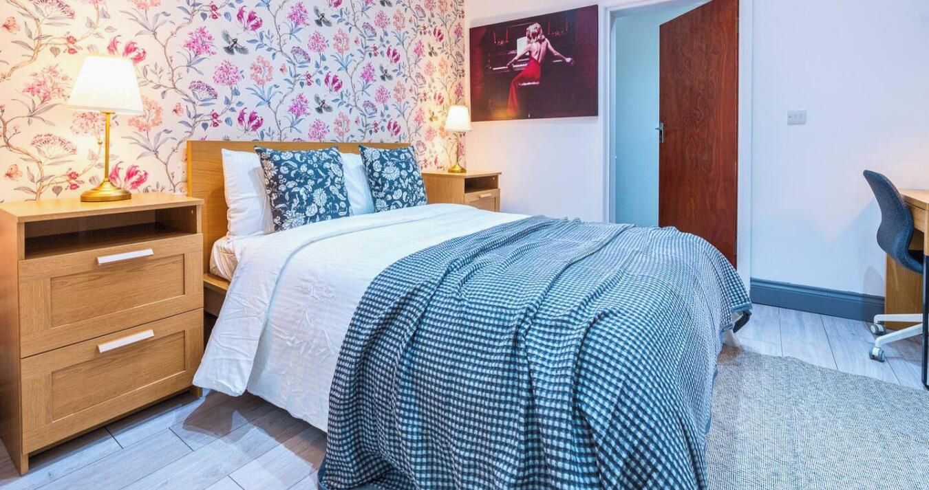 A bedroom with a bed, two bedside tables, a lamp, a poster on the wall, and a chair.