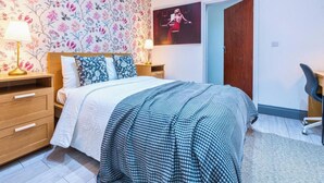 A bedroom with a bed, two bedside tables, a lamp, a poster on the wall, and a chair. - Stylish 3BR | 3 En-Suite Showers | Sleeps 8 (Greater London)
