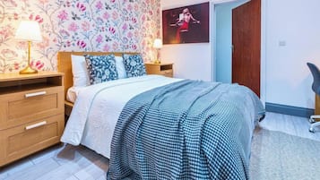 A bedroom with a bed, two bedside tables, a lamp, a poster on the wall, and a chair.