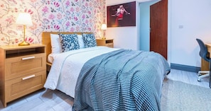 A bedroom with a bed, two bedside tables, a lamp, a poster on the wall, and a chair. - Stylish 3BR | 3 En-Suite Showers | Sleeps 8 (Greater London)