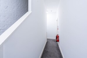 A narrow hallway with white walls, a grey carpet, and a fire extinguisher mounted on the wall. - Farringdon Loft | Balcony | Sleeps 4 | Zone 1 (Greater London)
