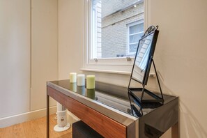 A room with a piano, a small table with candles, and a window with a view of a brick building. - Fitzrovia Apartments | 3BR | Sleeps 18 | Oxford-1 (Greater London)