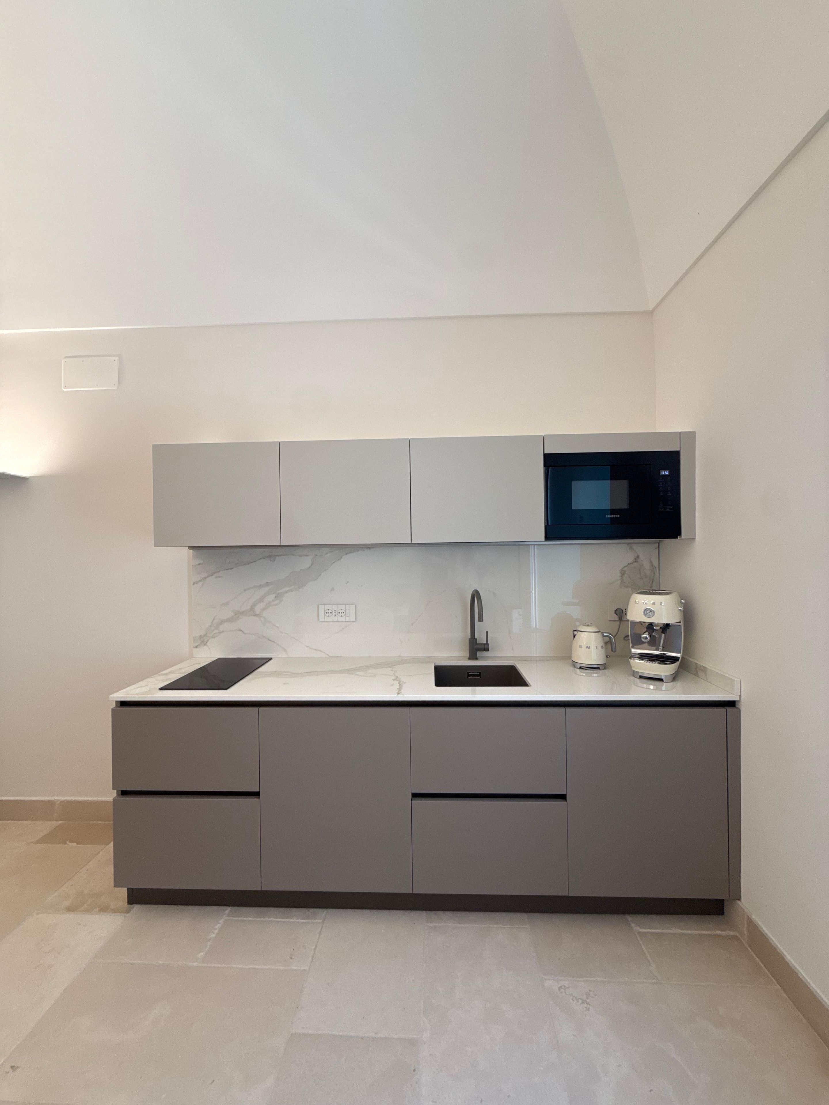 A modern kitchen with grey cabinets, a built-in microwave, a coffee machine, and a tablet on the countertop.
