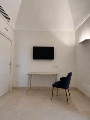 Ein Zimmer mit einem wandmontierten Flachbildfernseher, einem weißen Schreibtisch und einem dunkelblauen Stuhl.
