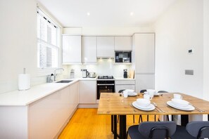 Eine moderne Küche mit weißen Schränken, einem Holztisch gedeckt mit Tellern und Tassen, und einem Fenster, das für natürliches Licht sorgt.