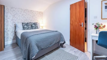 A bedroom with a bed, a bedside table, a chair, a wooden door, and a wall with a floral pattern.