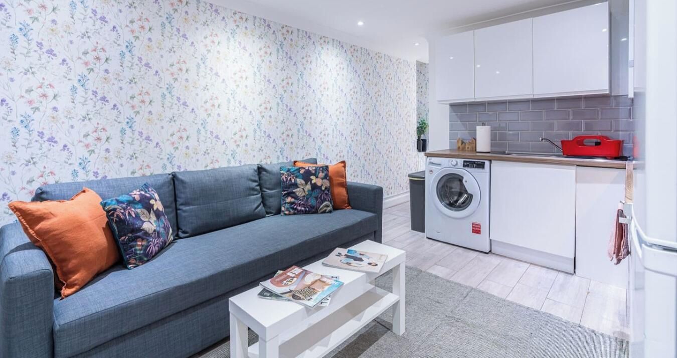 A modern living room with a sofa, a coffee table, and a washing machine in the background.
