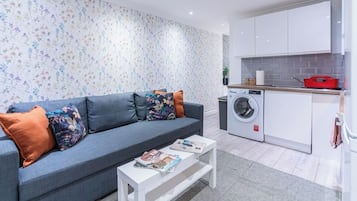 A modern living room with a sofa, a coffee table, and a washing machine in the background.