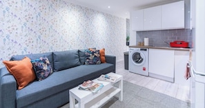 A modern living room with a sofa, a coffee table, and a washing machine in the background. - Stylish 3BR | 3 En-Suite Showers | Sleeps 8 (Greater London)