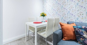 A dining area with a white table, four chairs, and a vase with yellow flowers. - Stylish 3BR | 3 En-Suite Showers | Sleeps 8 (Greater London)