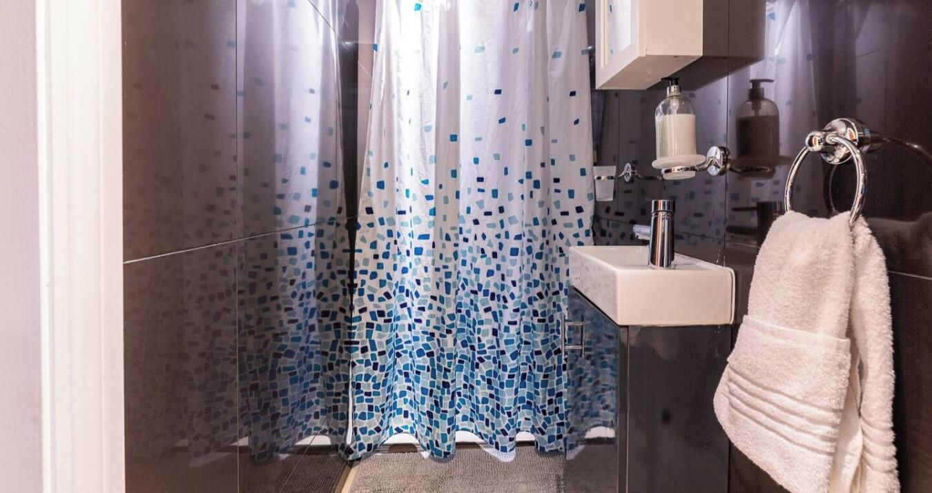 A bathroom with a shower curtain, a sink, and a towel rack.