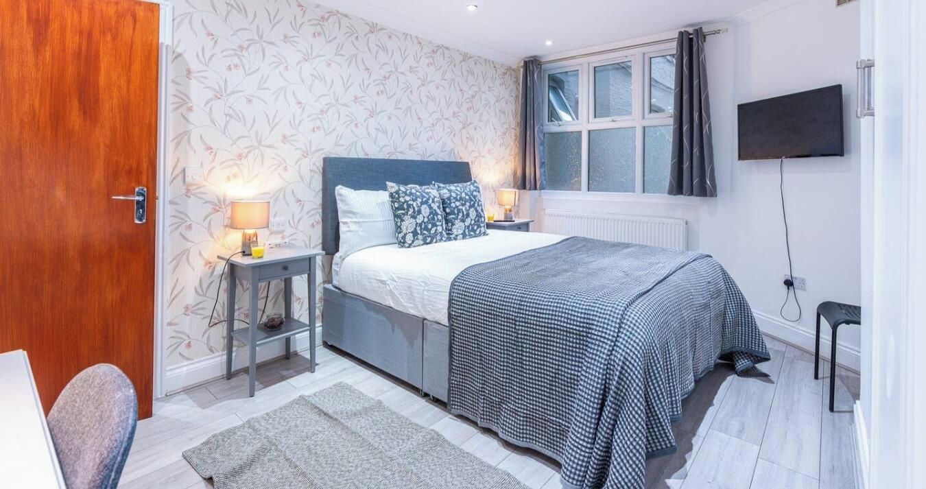 A bedroom with a bed, bedside tables, a TV, and a window with curtains.