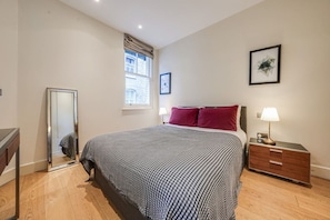 A bedroom with a bed, bedside table, lamp, and a mirror. - Fitzrovia 1BR Retreat | Near Soho & Tube-6 (Greater London)