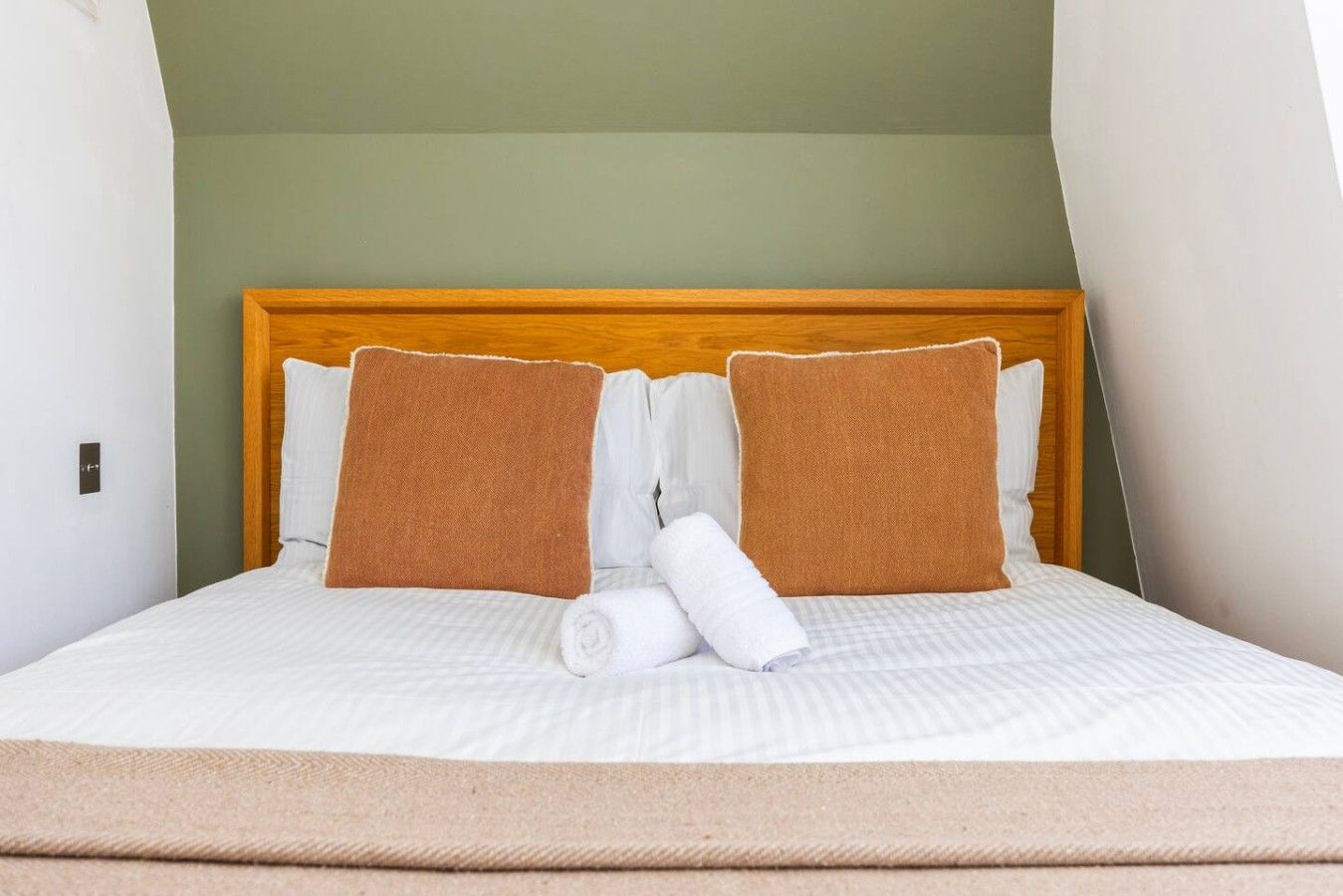 A bed with a wooden headboard, two brown pillows, and a white blanket rolled at the foot.