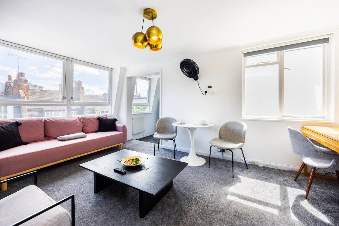 Ein modernes Wohnzimmer mit einer Couch, einem Couchtisch und Sesseln, einem Esstisch und einem großen Fenster mit Blick auf Gebäude.