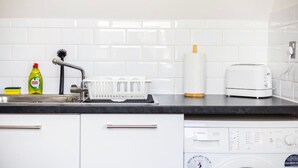 A kitchen with a white tiled backsplash, a Bosch dishwasher, a white toaster, a dish rack, a dish soap bottle, and a dish brush. - Elegant 1BR | Balcony | Knightsbridge & Hyde Park (Greater London)