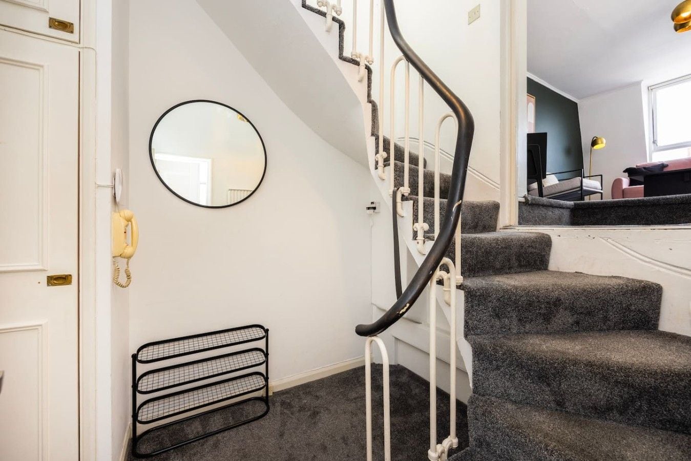 A staircase with a handrail, a round mirror, and a radiator on the wall.