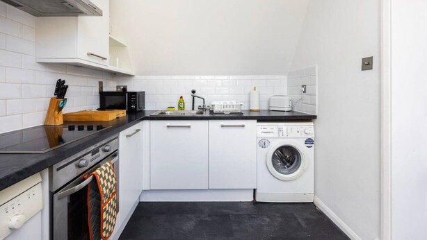 A compact kitchen with a dishwasher, microwave, and a sink. - Elegant 1BR | Balcony | Knightsbridge & Hyde Park (Greater London)