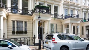 A white SUV parked in front of a building with white columns and balconies. - Elegant 1BR | Balcony | Knightsbridge & Hyde Park (Greater London)