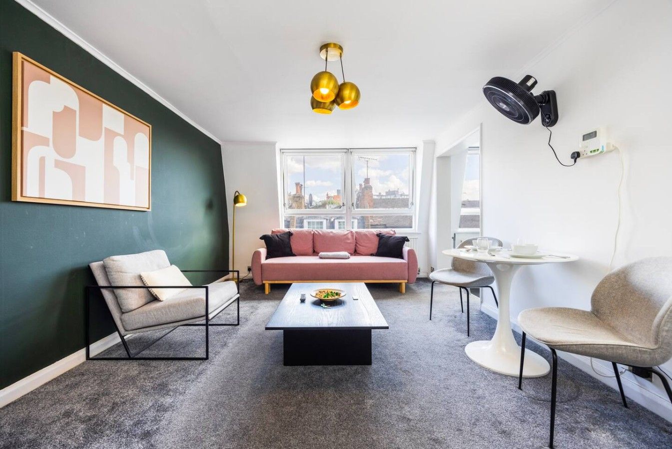 En moderne stue med sofa, lænestole, sofabord og udsigt over byen gennem store vinduer.