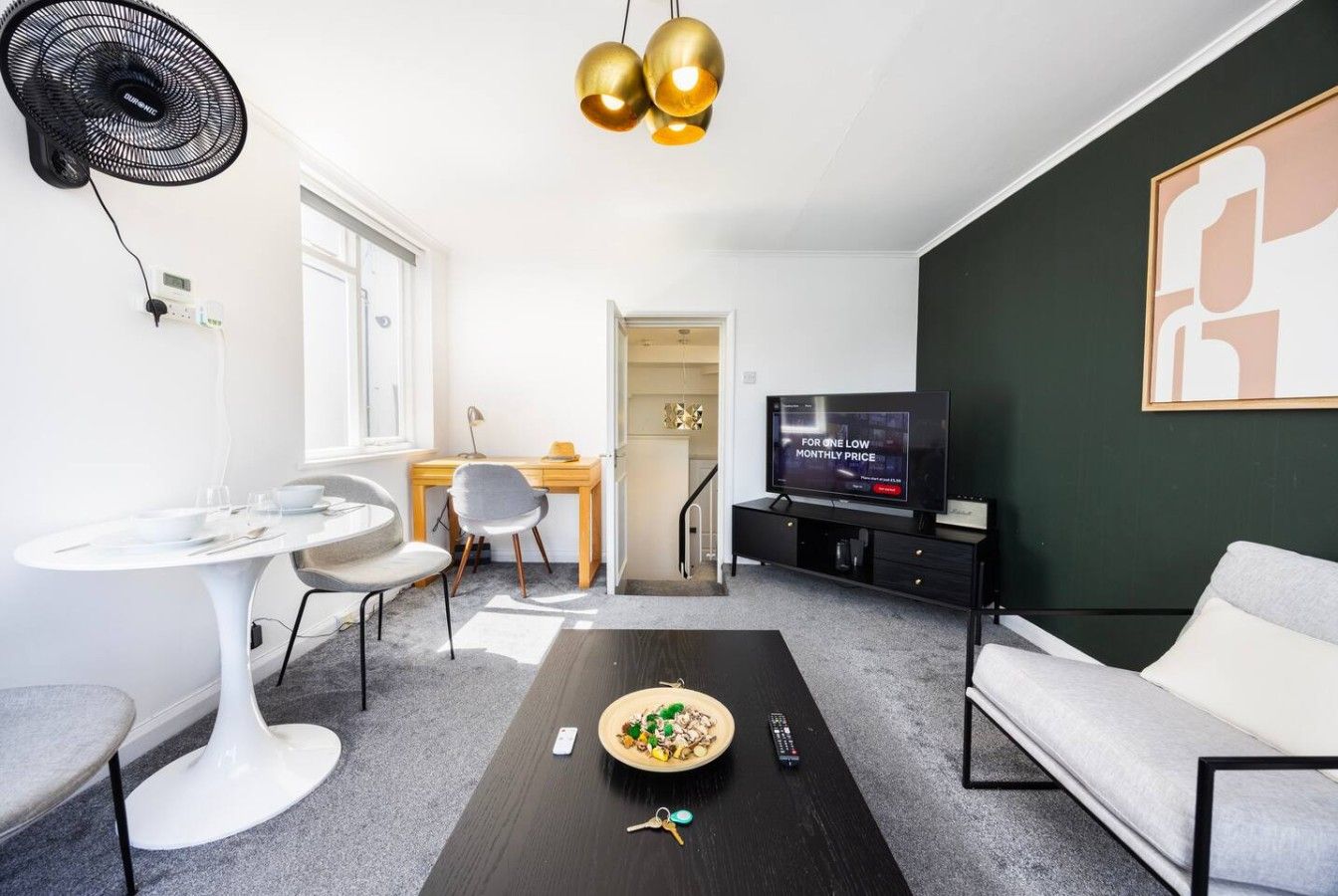 Ein modernes Wohnzimmer mit Esstisch, einer Couch, einem Fernseher und einem Deckenventilator.
