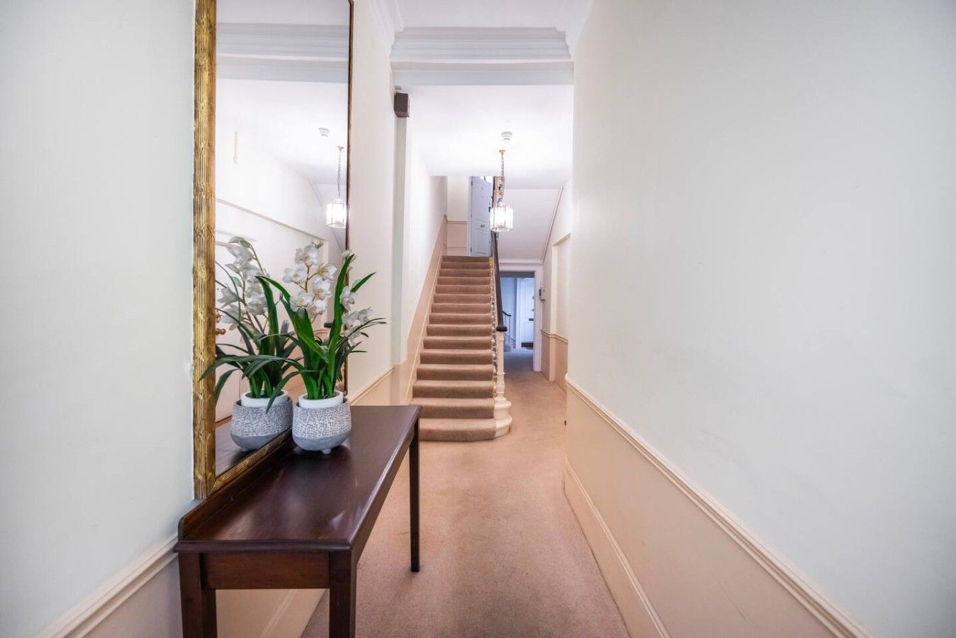 Ein Flur mit einer hölzernen Bank, Zimmerpflanzen, einer Treppe und einem Spiegel an der Wand.