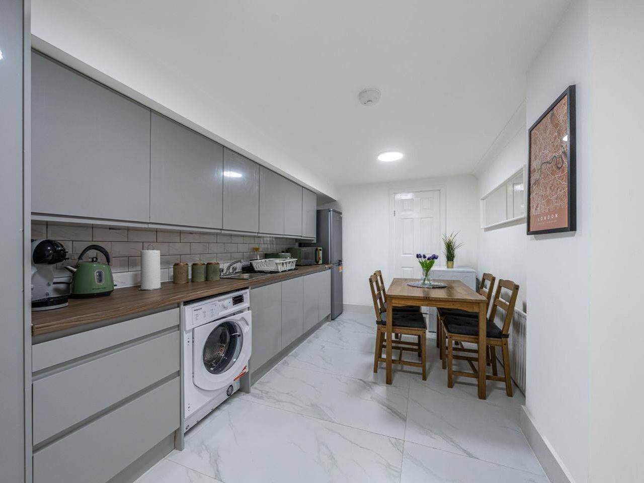 A modern kitchen with grey cabinets, a washing machine, and a dining area with a table and chairs.
