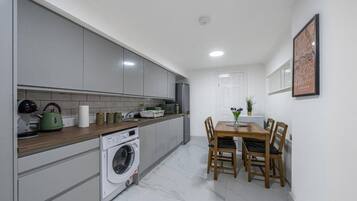 A modern kitchen with grey cabinets, a washing machine, and a dining area with a table and chairs.
