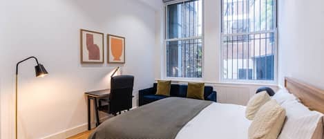 Un dormitorio moderno con cama, escritorio, silla y dos ventanas.