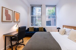 A bedroom with a bed, a desk, a chair, a window, and two framed pictures on the wall. - Farringdon 1BR | Sleeps 6 | Elizabeth Line Direct (Greater London)