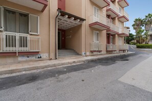 Ein mehrstöckiges Wohngebäude mit Balkonen, einem überdachten Eingang und Blick auf die Straße.