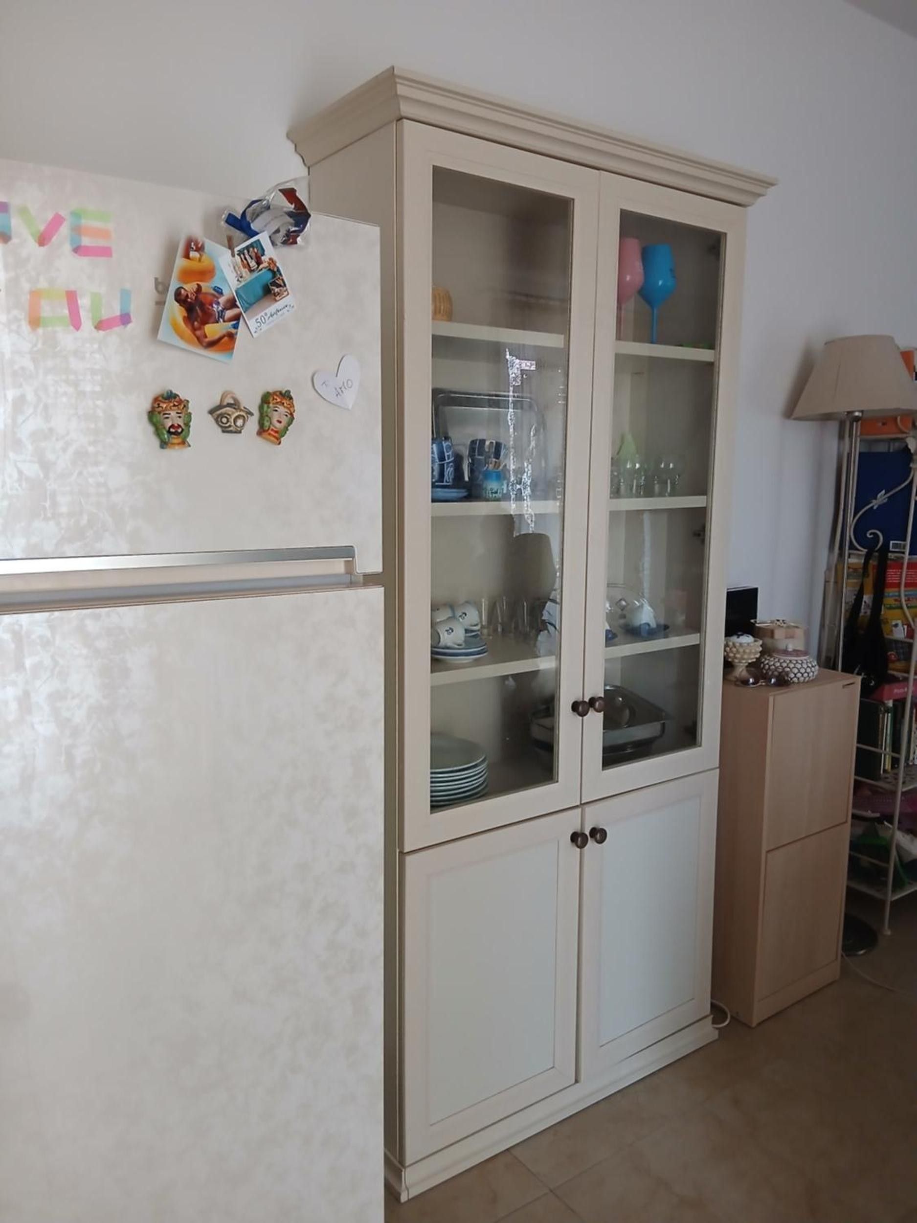 Une cuisine avec un réfrigérateur blanc, un meuble avec des portes en verre et une lampe.