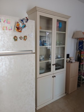 Une cuisine avec un réfrigérateur blanc, un meuble avec des portes en verre et une lampe.