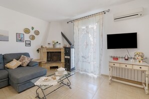 Ein Wohnzimmer mit einer Couch, einem Glastisch mit Dekoration, einem Kamin, einem Fernseher und einer weißen Wand mit dekorativen Tellern.