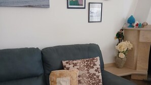 Ein Wohnzimmer mit einem dunkelgrünen Sofa, einem gemusterten Kissen und einem gerahmten Bild an der Wand.