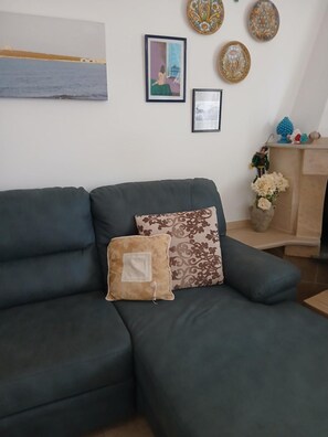 Un salon avec un canapé vert foncé, un coussin à motifs et un tableau encadré accroché au mur.