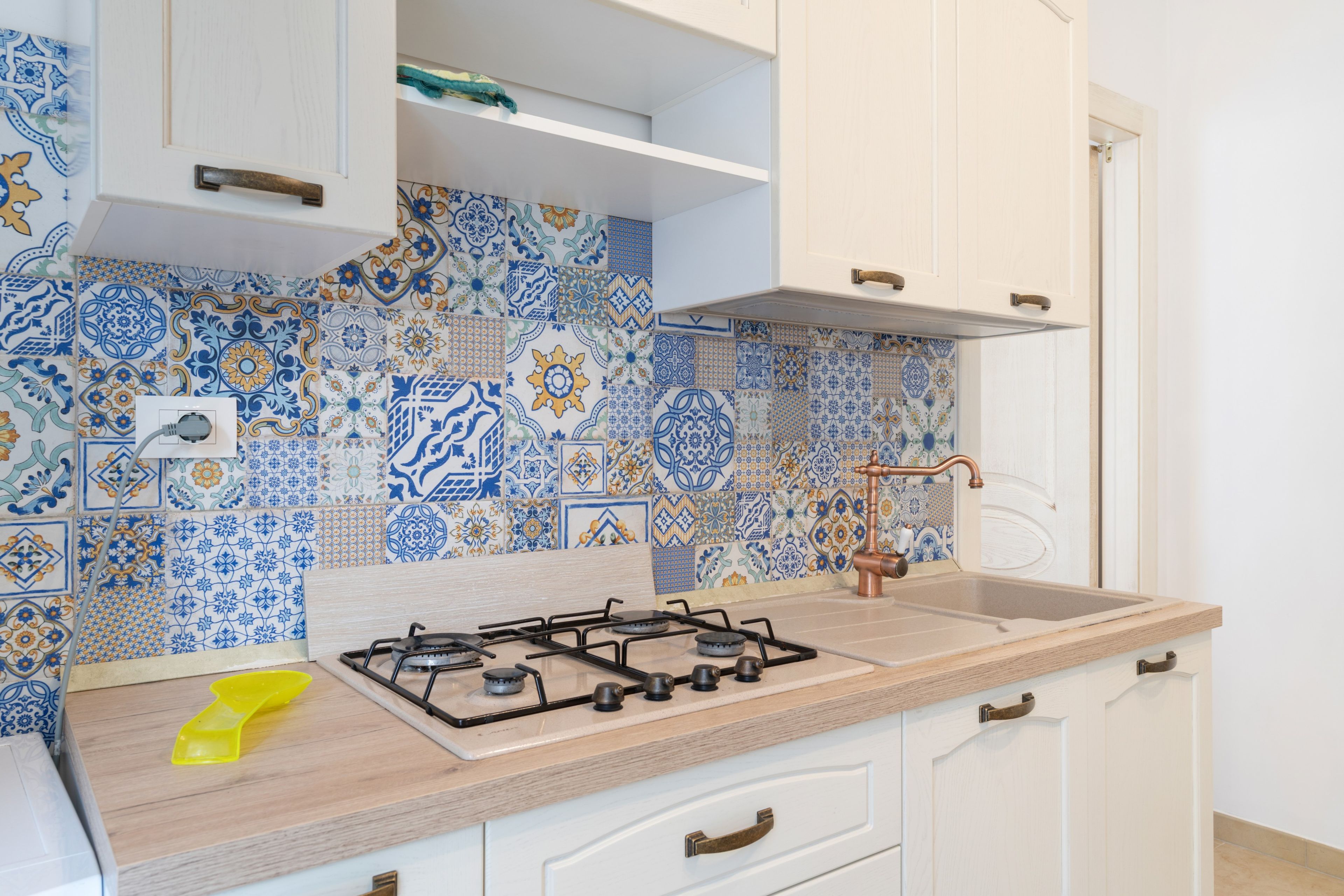 Una cucina con piano cottura a gas, lavello e schienale rivestito di piastrelle bianche e azzurre.