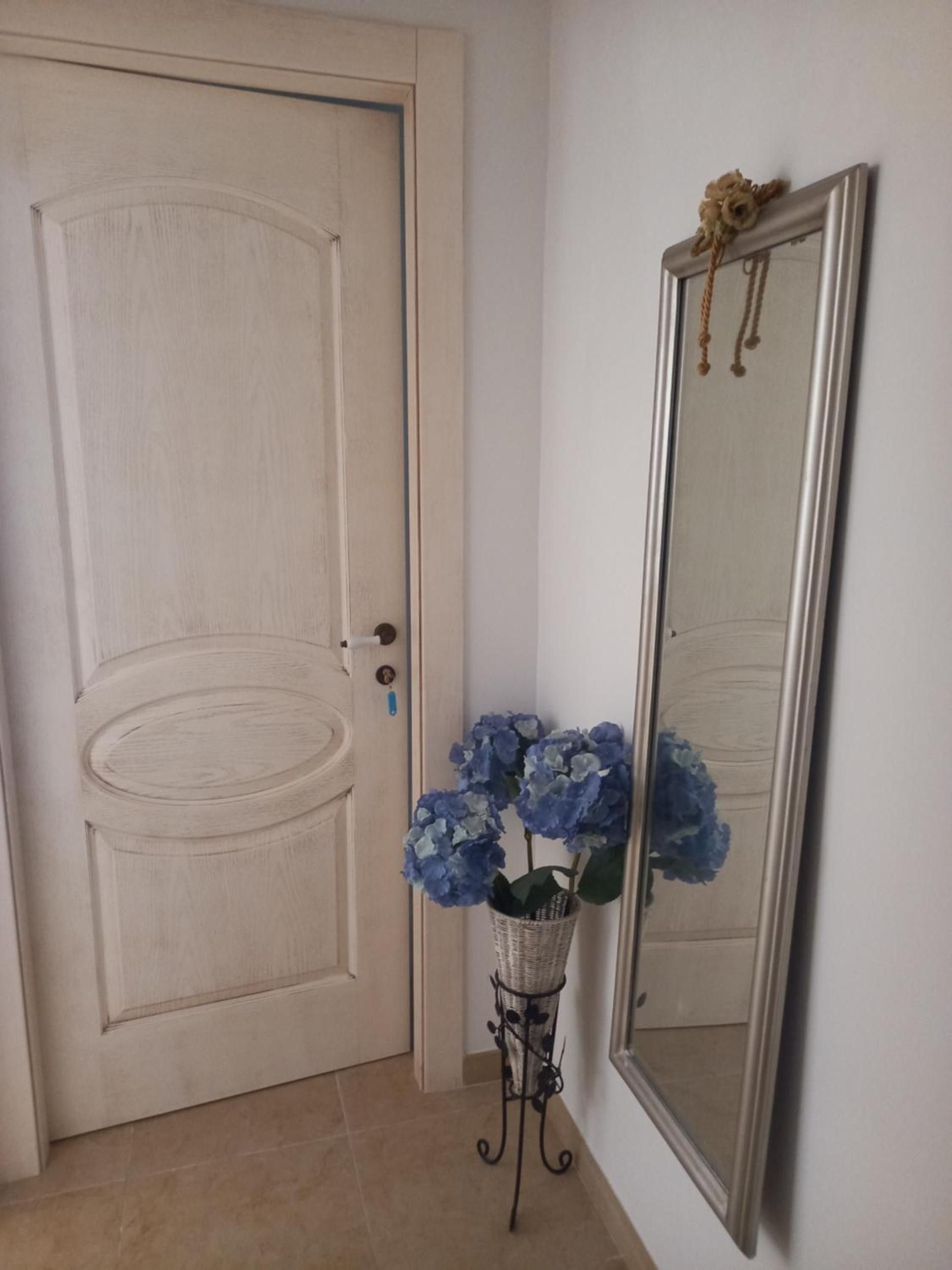 Una porta con una serratura, uno specchio con una cornice decorativa e un cesto di fiori.