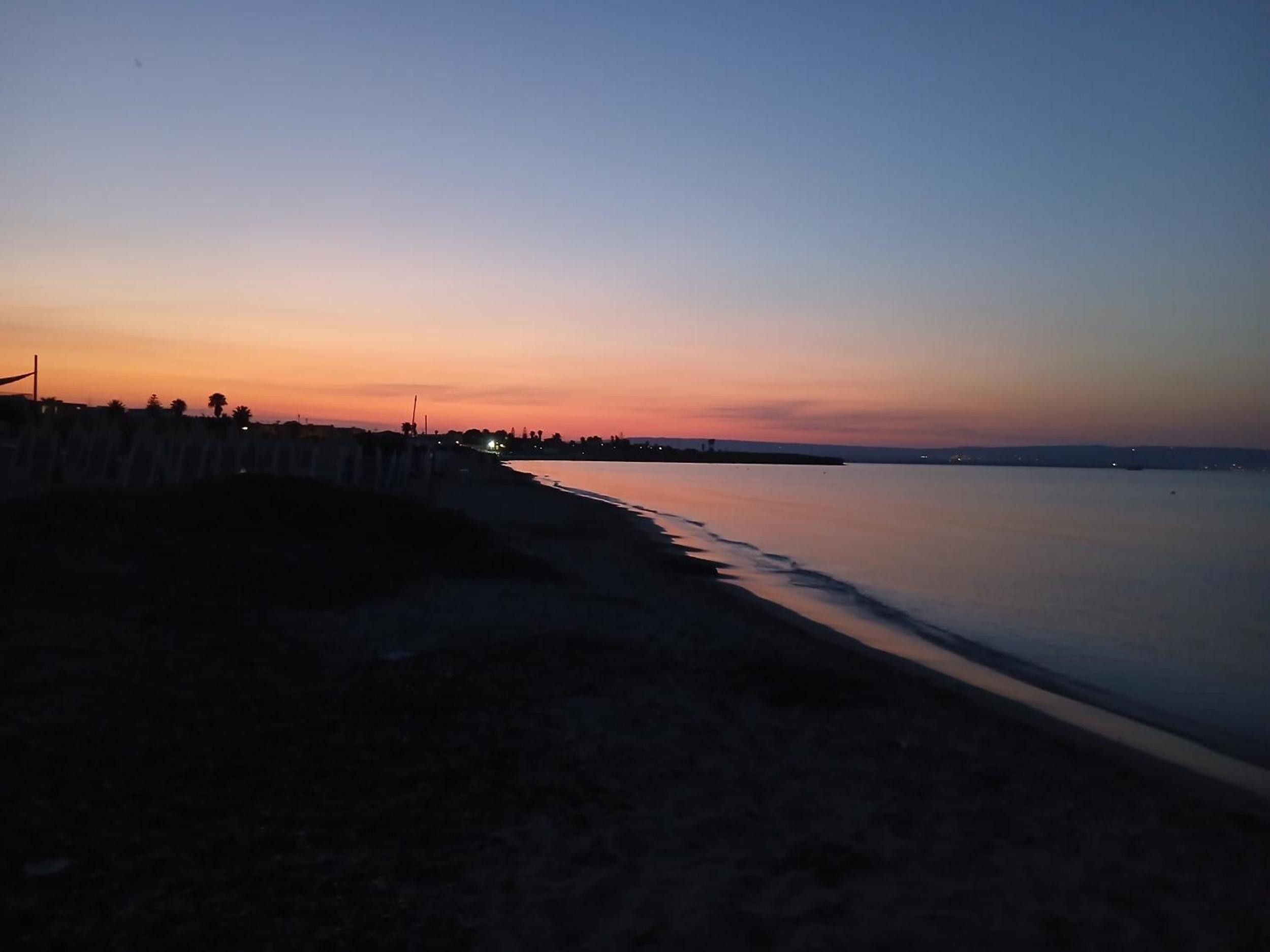 Une plage au crépuscule, avec une mer calme et une côte lointaine.