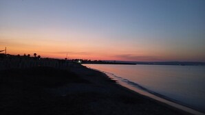 Ein Strand im Dämmerlicht mit ruhiger See und einer fernen Küste.